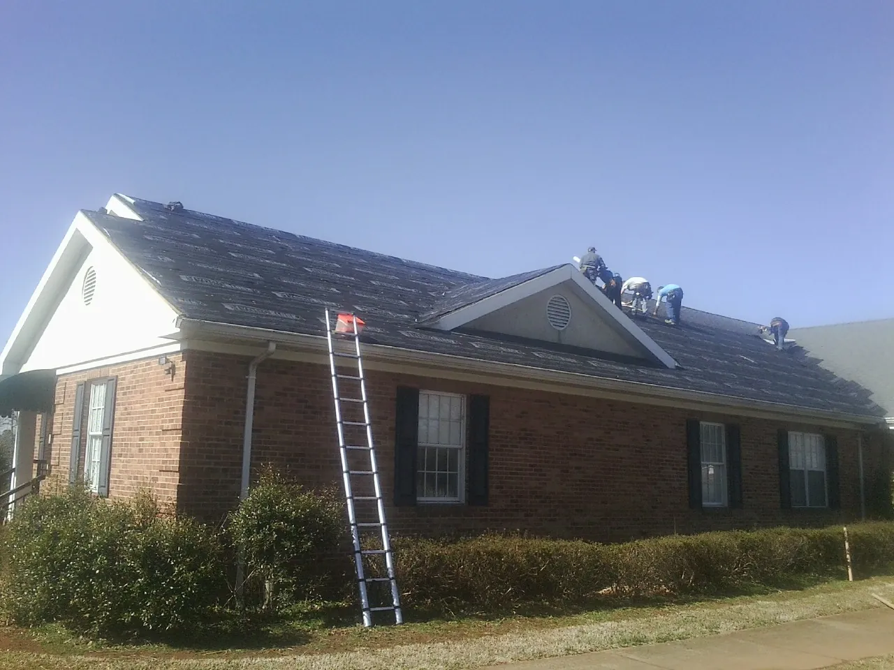 Crew tearing shingles off a brick ranch roof with a ladder set — Emergency Roof Repair work by our crew in Morris Plains