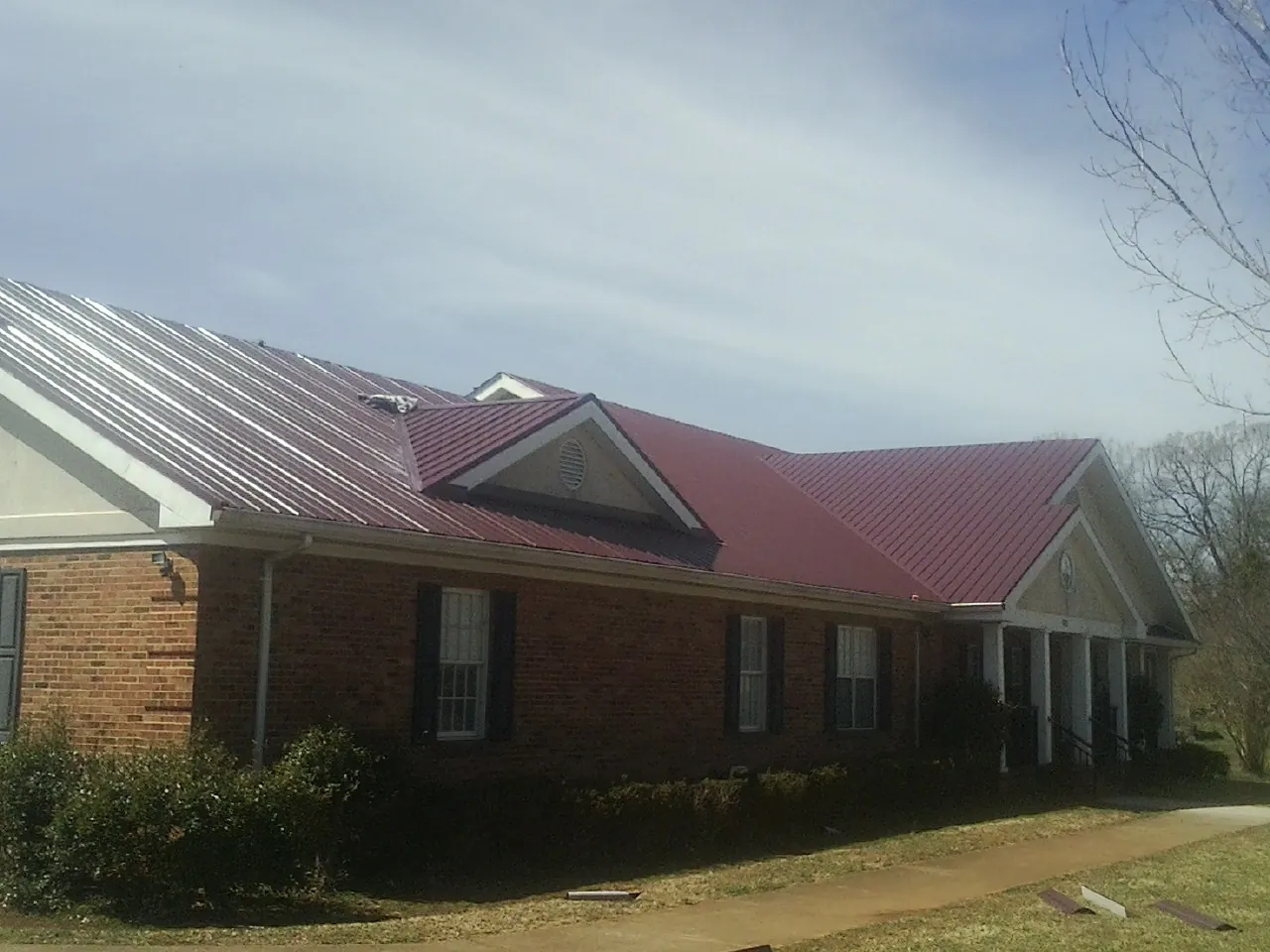 Red metal roof with gabled entries on a long brick building, from a Hail Damage Roof Repair job in Morris Plains