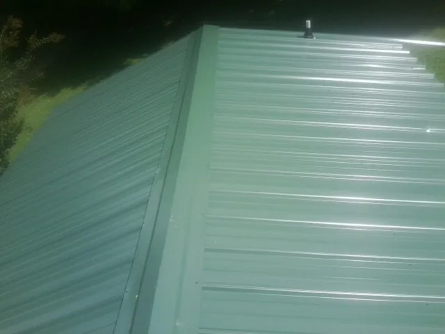 New green metal panels meeting at the ridge of a roof — Flat Roof Repair work by our crew in Morris Plains