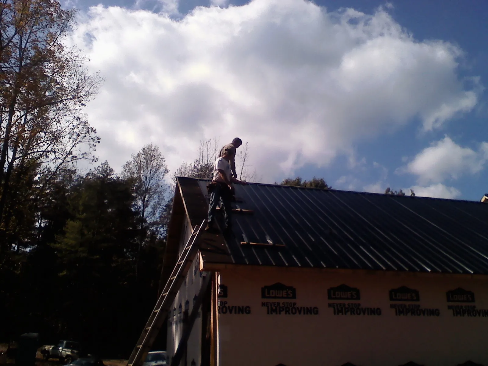 Roofer fastening dark metal panels high against a cloudy sky, from a Roof Inspection job in Morris Plains