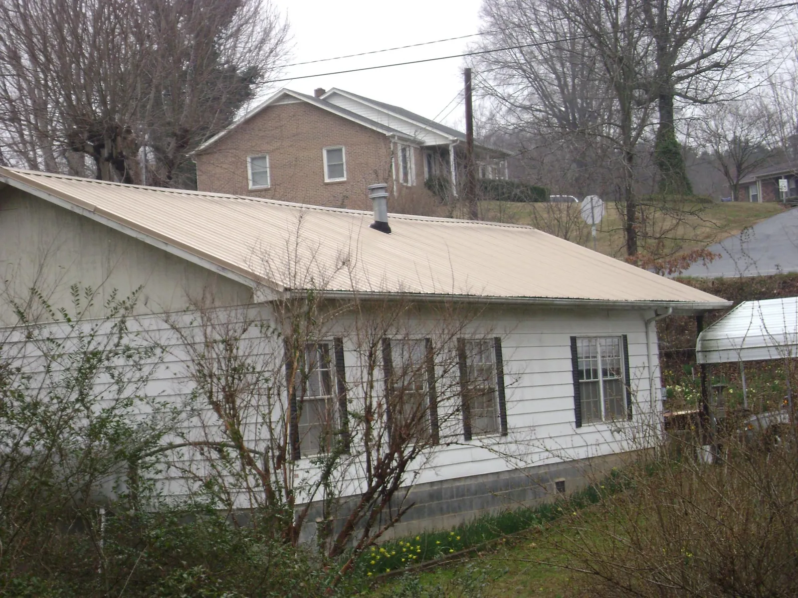 Tan metal roof on a white sided house set into a hillside — Commercial Roofing by Roofing Brothers in Morris Plains